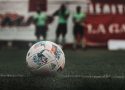 A detailed view of a soccer ball on a grass field with players blurred in the background.