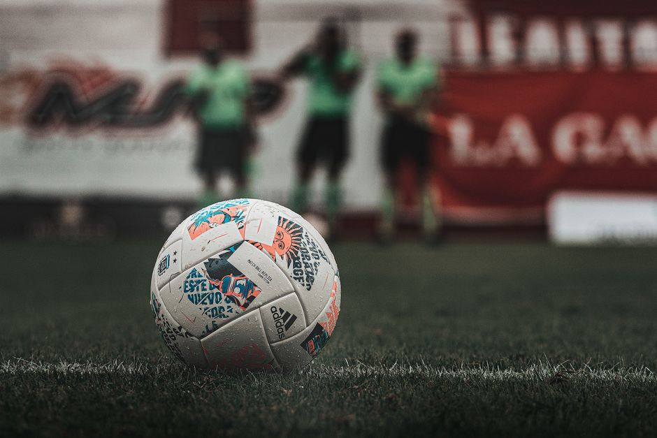 A detailed view of a soccer ball on a grass field with players blurred in the background.
