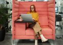 Businesswoman in a yellow sweater working on a laptop in a modern office booth setting, exhibiting style and focus.